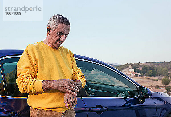 Älterer Reisender  der in der Nähe des Autos die Zeit kontrolliert