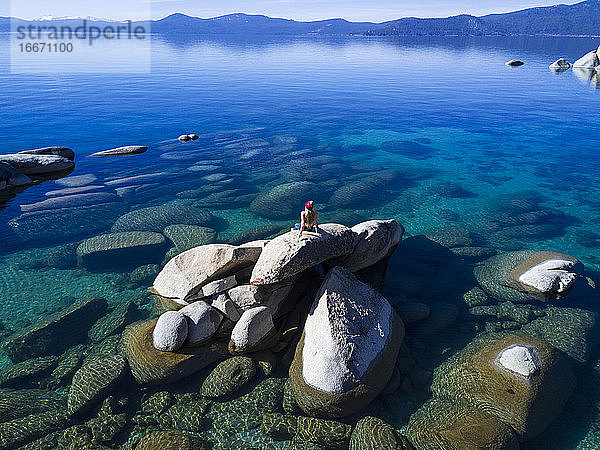 Frau betrachtet die Aussicht  während sie auf einem Felsen am Lake Tahoe sitzt