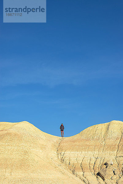Vorderansicht einer Frau auf einem Hügel  die mit den Händen in den Taschen steht und zum Horizont schaut