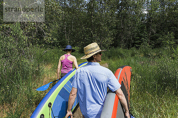 Ein junges Paar trägt Standup-Paddleboards zum Wasser in Oregon.