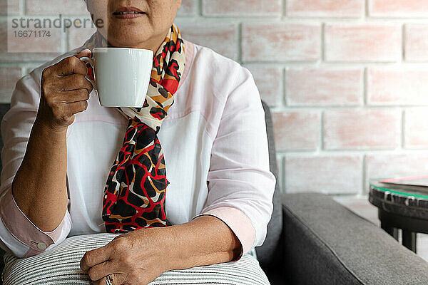 Alte Frau hält eine Tasse heißen Kaffee zu Hause trinken