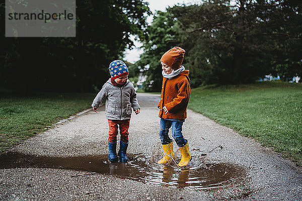 Männliche Kinder  die an einem regnerischen Tag im Park in die Pfützen springen