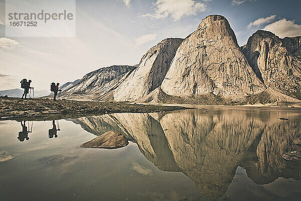 Silhouettierte Reflexion von zwei Rucksacktouristen gegenüber einer Berglandschaft.