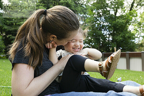 Mutter umarmt glückliche lachende Kleinkind-Tochter  während sie im Freien sitzt