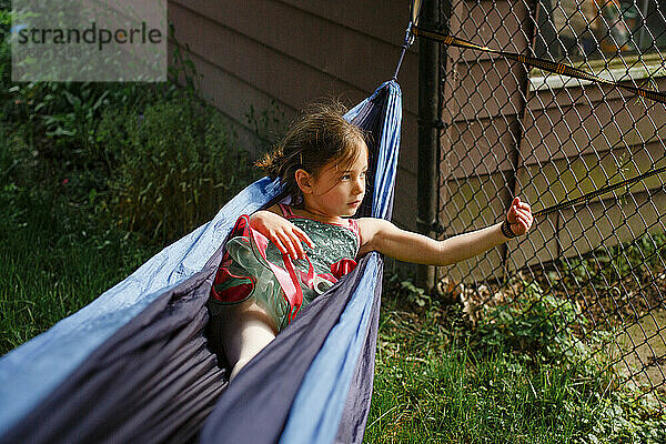 Ein kleines Mädchen in einem bunten Tutu spielt in einer Hängematte im Sonnenschein