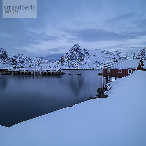 Olstind-Gipfel und rote Rorbu-Hütten  die sich über der schneebedeckten Küste erheben  Moskenesøy  Lofoten  Norwegen