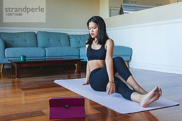 Frau benutzt digitales Tablet  um zu Hause Yoga zu praktizieren