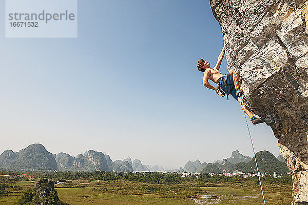 Männlicher Kletterer zieht sich an einem überhängenden Felsen in Yangshuo / China hoch