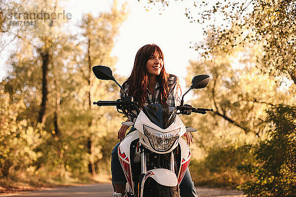 Lächelnde  selbstbewusste junge Frau auf einem Motorrad auf einer Landstraße sitzend