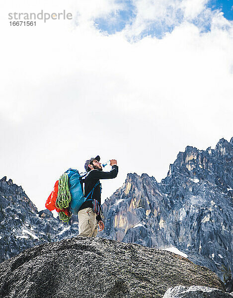 Mann trinkt Wasser auf Klettertour mit Bergen im Hintergrund