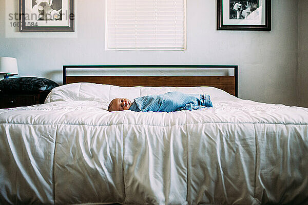 Neugeborenes schläft allein auf großem Bett