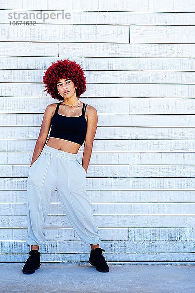 Frau mit rotem Afro-Haar  die an einer weißen Wand steht.