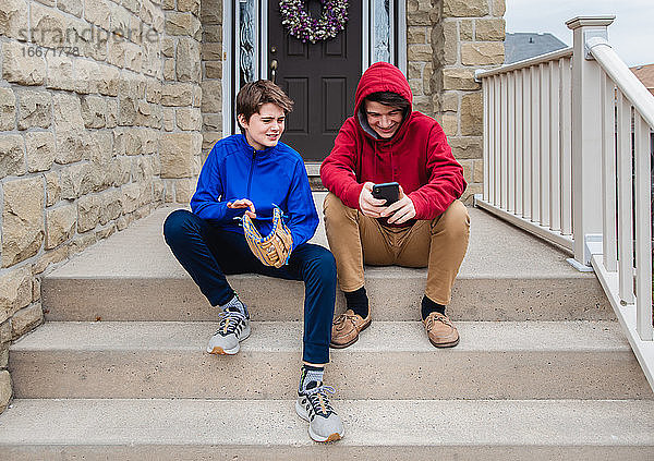 Zwei Teenager sitzen auf der Treppe eines Hauses und unterhalten sich.