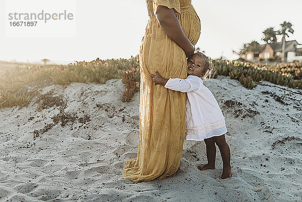 Seitenansicht eines Kleinkindes  das den schwangeren Bauch seiner Mutter umarmt