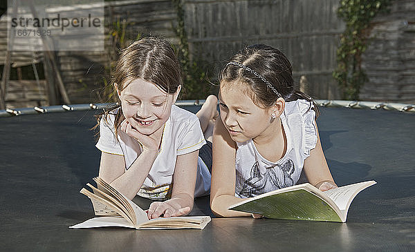 zwei Freunde liegen auf einem Trampolin und lesen Bücher in Woking