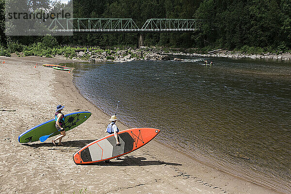 Ein junges Paar trägt Standup-Paddleboards zum Wasser in Oregon.