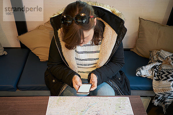 Frau sitzt vor einer Touristenkarte und schaut auf ihr Telefon