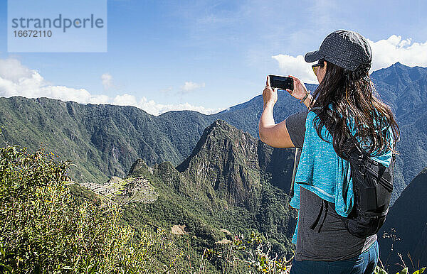Eine Frau fotografiert mit ihrem Smartphone Machu Picchu auf dem Inka-Pfad