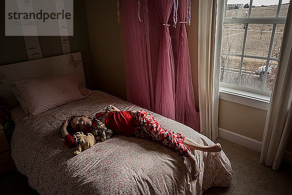 ein gelangweiltes junges Mädchen liegt auf ihrem Bett in ihrem Schlafzimmer in der Nähe des Fensters