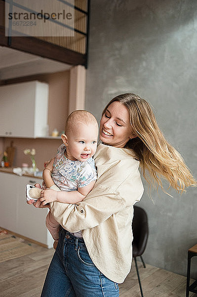 Lächelnde Frau hält in den Händen Baby-Mädchen im Wohnzimmer. Kindermädchen  Kind.