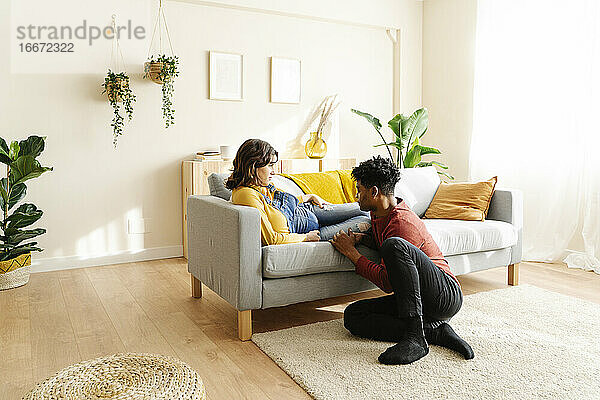 Ehemann streichelt den Bauch seiner schwangeren Frau auf einem Sofa. Interracial Paar Konzept