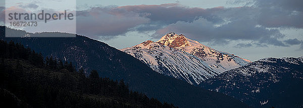 An einem Frühlingstag in den Coast Mountains von British Columbia geht die Sonne über den schneebedeckten Bergen unter.