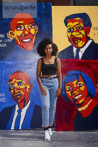 Eine schöne junge Künstlerin steht stolz vor ihrem Wandgemälde