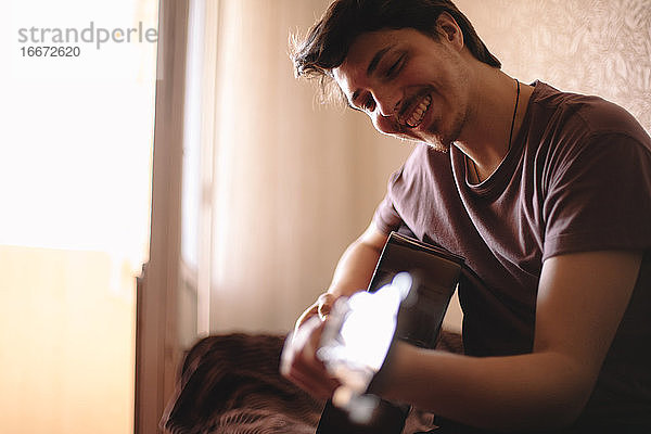 Glücklicher junger Mann spielt zu Hause Gitarre