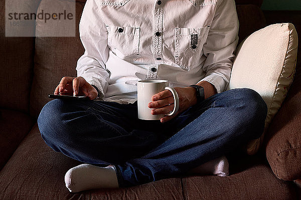 Nahaufnahme eines jungen Mannes  der auf sein Smartphone schaut  während er auf einer Couch sitzt