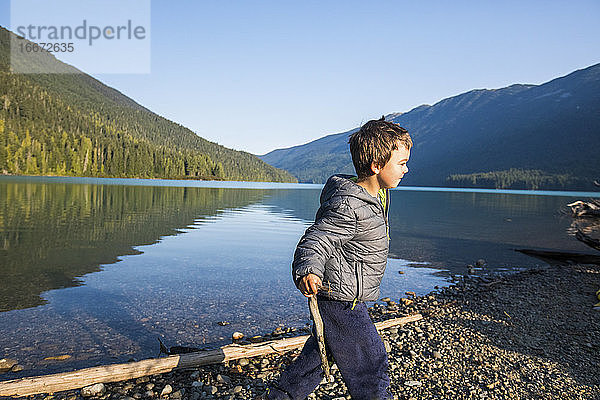 Junge spielt mit Stöcken in der Natur  Seeufer  malerische Aussicht.