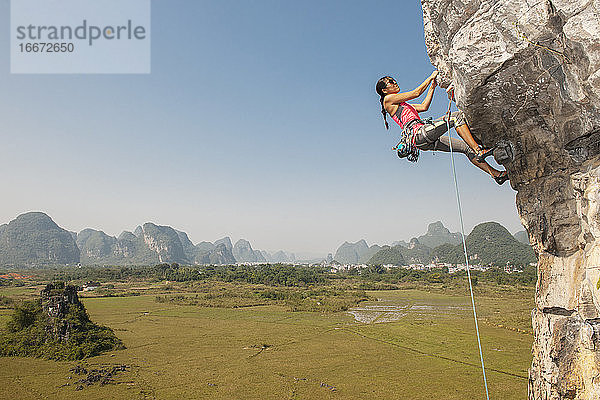Bergsteigerin zieht sich an einem überhängenden Felsen in Yangshuo / China hoch
