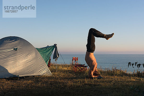 Erwachsener Mann macht Yoga bei Sonnenaufgang  vor dem Zelt am Meer