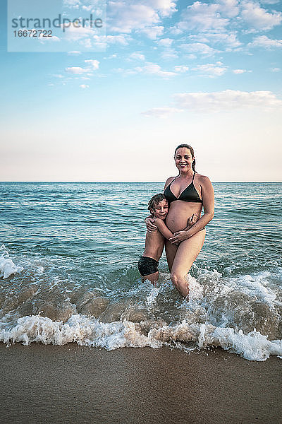 5 Jahre altes Kind  das seine schwangere Mutter umarmt  knietief im Meer