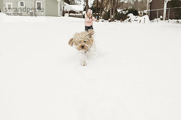 Junges Mädchen jagt ihren Hund durch den Schnee im Hinterhof