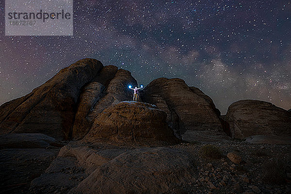 Ein Mann  der nachts in einer Felsenschlucht mit Blick auf die Milchstraße eine Lampe in der Hand hält