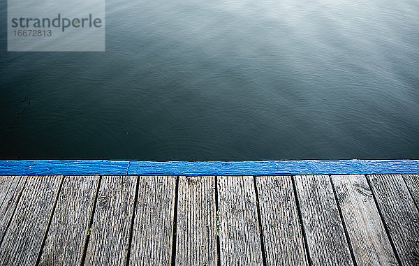 Rand eines leeren hölzernen Stegs gegen ruhiges blaues Seewasser.