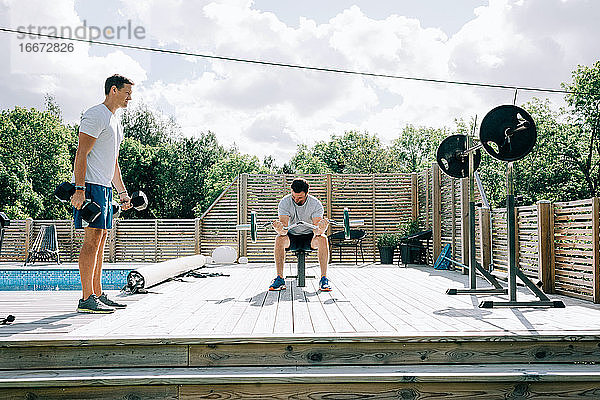 Zwei Freunde trainieren gemeinsam in ihrem Haus am Pool im Fitnessstudio