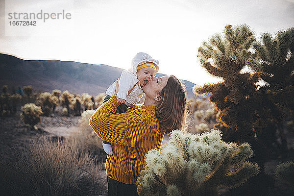 Eine Frau mit einem Baby steht in der Nähe eines Kaktus in der Wüste