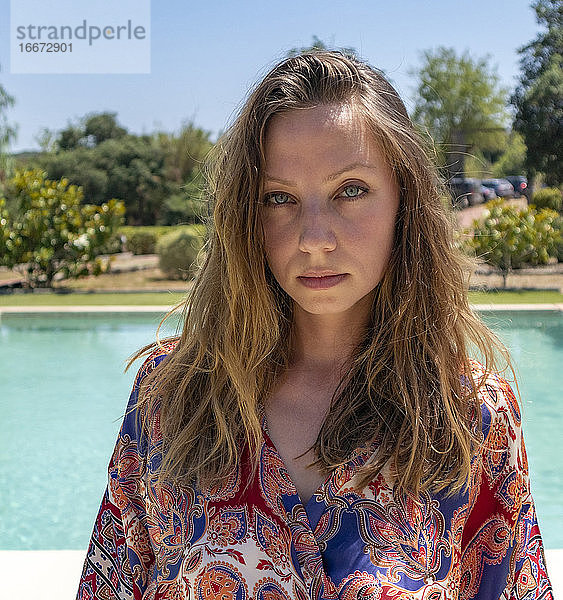 Blondes Mädchen posiert im Sommer mit einem Kleid am Pool