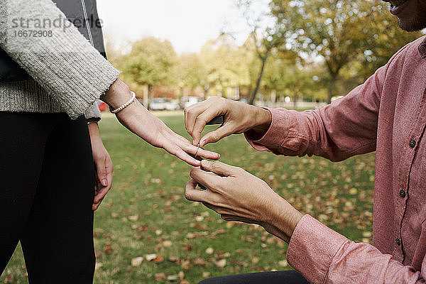 Kniender Mann  der seiner Freundin mit einem Ring in einem Park die Ehe anbietet. Liebe Konzept
