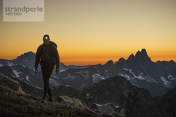 Wanderer steigt nach Sonnenuntergang mit Stirnlampe auf einen Berg.