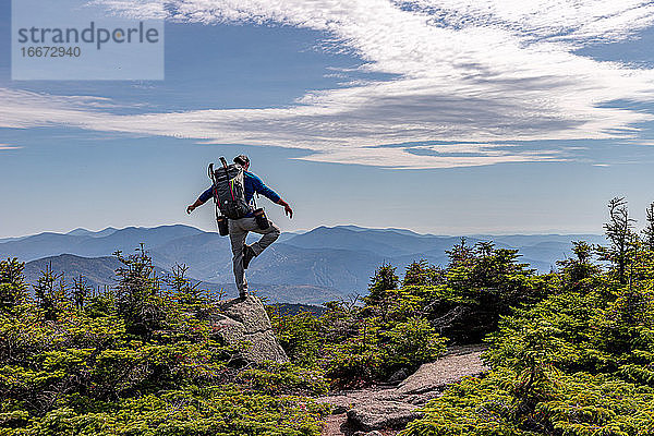 Mann übt Yoga und balanciert auf einem Bein auf dem Gipfel eines Berges.