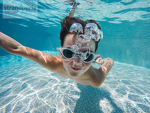 Unterwasserbild eines Jungen  der mit Schwimmbrille in einem Pool schwimmt.