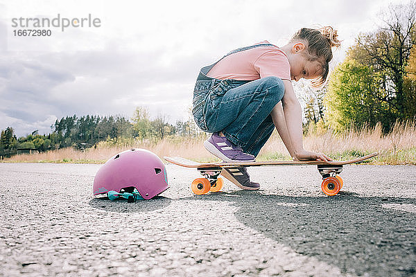 junges Mädchen sitzt auf einem Skateboard und lernt skaten
