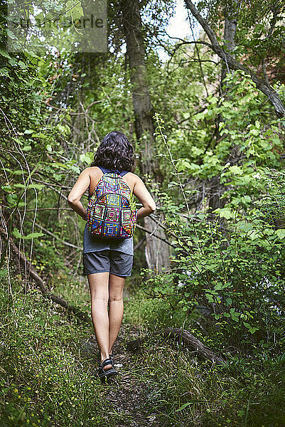 Junges Mädchen geht im Wald spazieren. Sie hat einen Rucksack auf dem Rücken.
