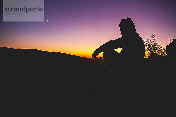 Silhouette eines Mannes mit Fernglas bei Sonnenuntergang mit dem Muh