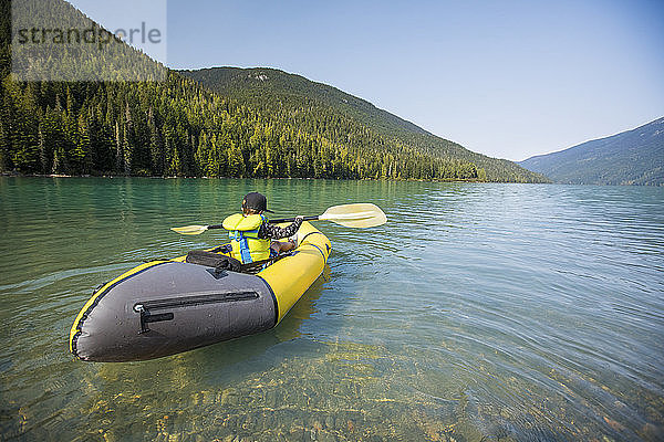 Rückansicht eines Jungen  der mit einem gelben Boot auf einem malerischen See paddelt.
