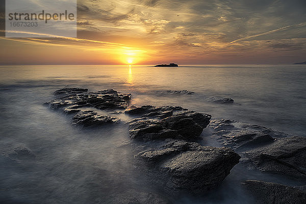 Schöner Sonnenuntergang an der Küste mit den Wellen  die über die Felsen laufen