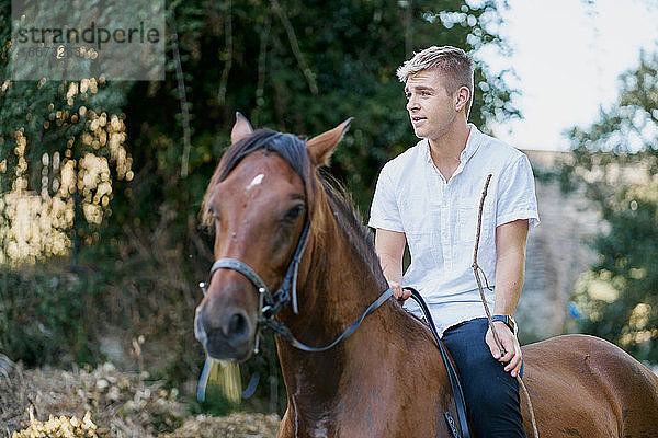 Porträt eines jungen blonden Mannes  der auf einem Pferd über einen Fluss reitet