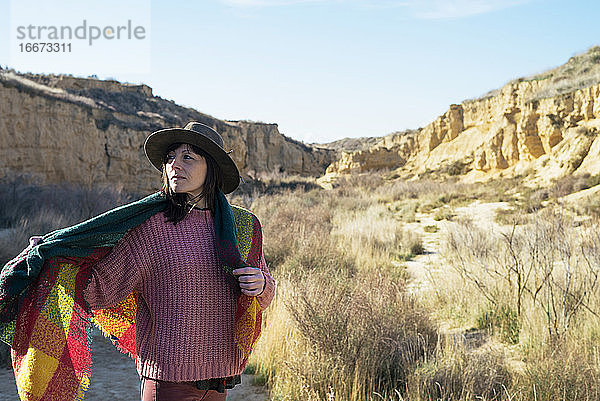 Frau mit Hut und Schal in einer Wüstenschlucht stehend